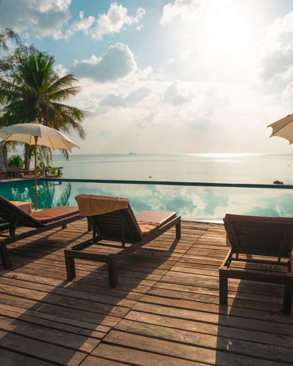 A serene beach scene with sun loungers, umbrellas, and a view of the ocean under a partly cloudy sky at sunset.
