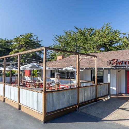 A small outdoor restaurant with a wooden fenced patio, red doors, and a sign that reads &ldquo;WAPPER,&rdquo; set beside a sunny, clear sky.