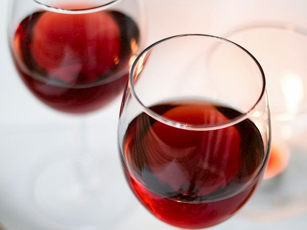 Two glasses of red wine on a table with a lavender bouquet, soft candlelight, and a light, airy backdrop.